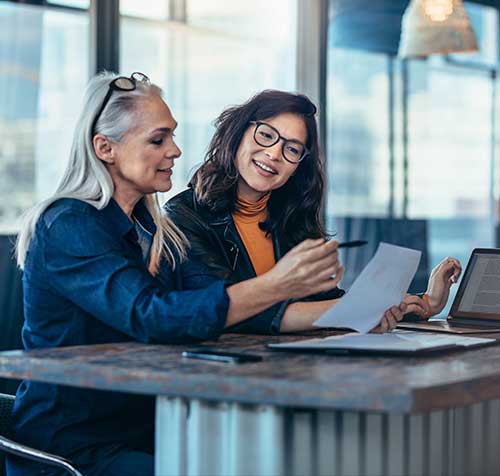 Dos mujeres sentadas en su escritorio y revisando un documento