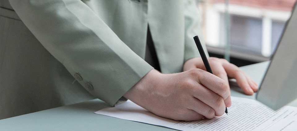Mujer empresaria de pie escribiendo en una hoja en su escritorio